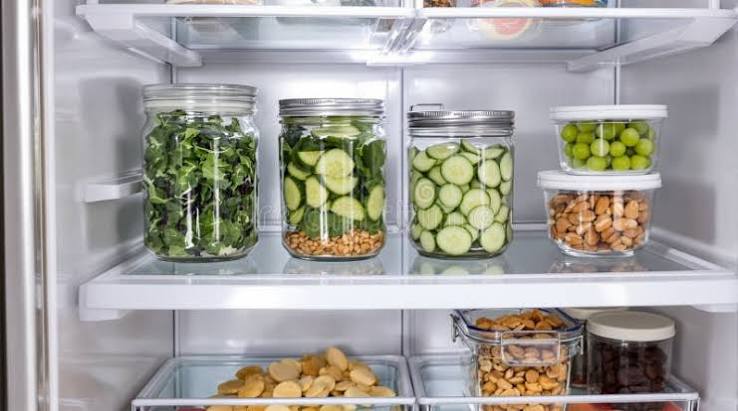 Organised fridge with glass jars of salad leaves and sliced cucumber
